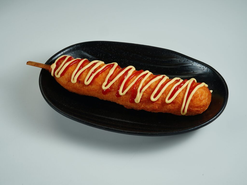 Corn dog posé sur une assiette avec ketchup et mayonnaise